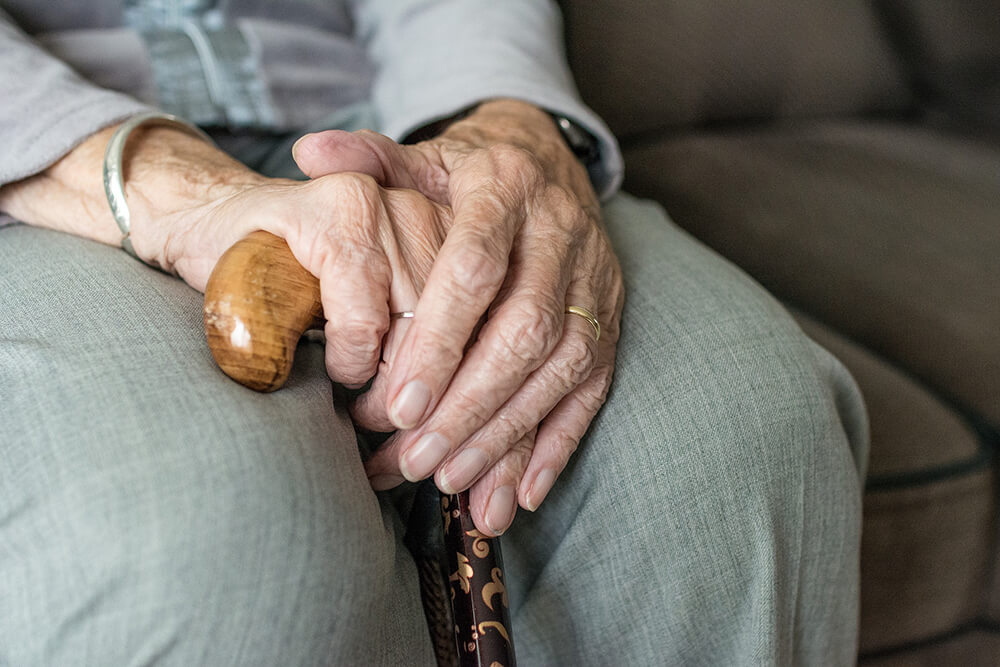 Elderly person's hands in their lap holding a cane